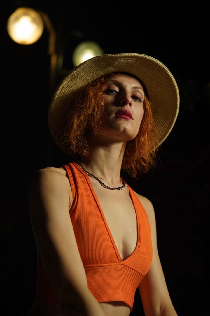 Low-angle portrait in a straw hat and orange top at night